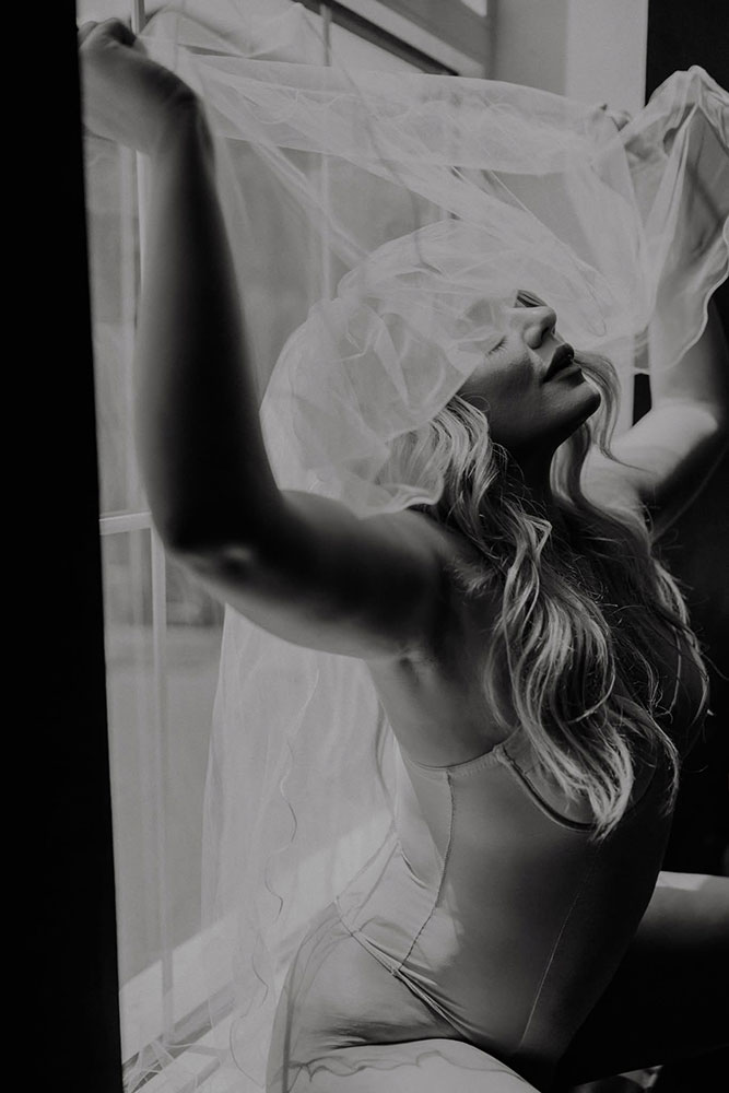 Nashville bridal boudoir studio image of bride sitting in a window with veil over face